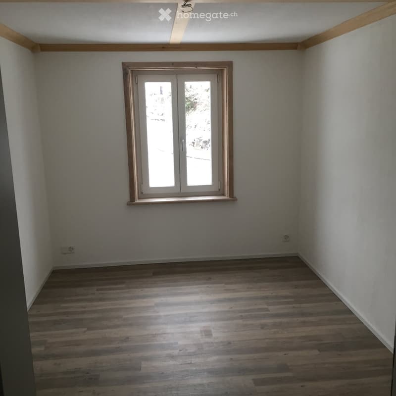 Empty room with wooden flooring, white walls, and a large window with double doors.