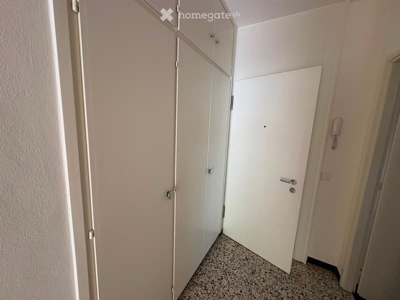 A narrow hallway with white walls, tiled floor, and two white doors with silver handles.