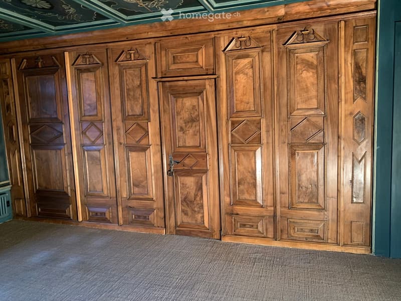A spacious hallway with ornate wooden paneling and doors, featuring intricate carvings and decorative elements.