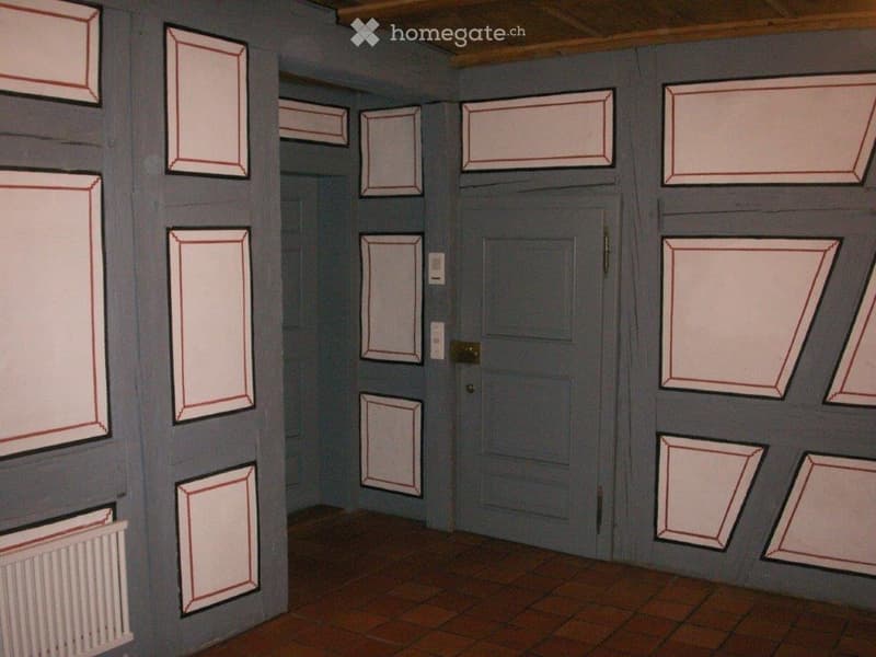{"type":"Room","description":"The image shows an interior room with gray walls and a wooden ceiling. The walls are decorated with various framed panels, creating a unique and artistic design. The room has a door in the center, and the floor appears to be