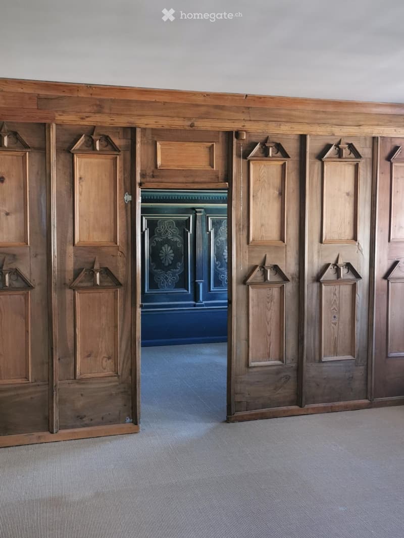 {"visible_features":[],"type":"Interior","description":"The image shows a wooden interior with ornate paneled walls and doors. The doors have decorative elements and the central doorway is painted in a deep blue color. The floor is covered with a gray car