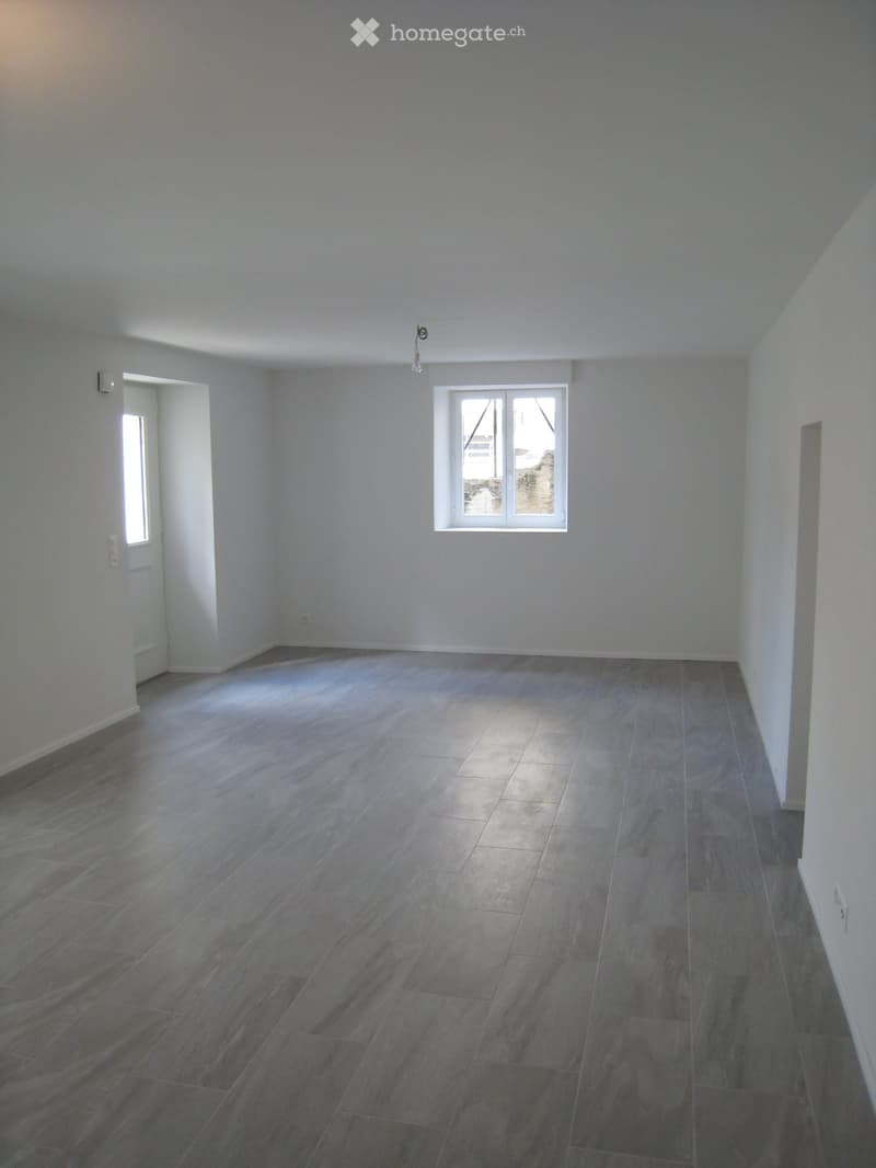 Empty room with light grey walls, dark grey tiled floor, and a single window with white frame. No furniture or equipment present.