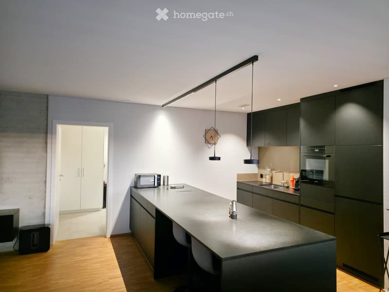 Modern kitchen with dark grey cabinets, a central island, and pendant lighting. Includes a microwave, oven, sink, and various small items on the counter.