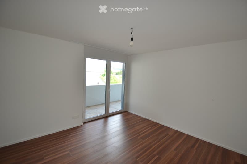 Empty room with wooden flooring, white walls, and a sliding glass door leading to a balcony.