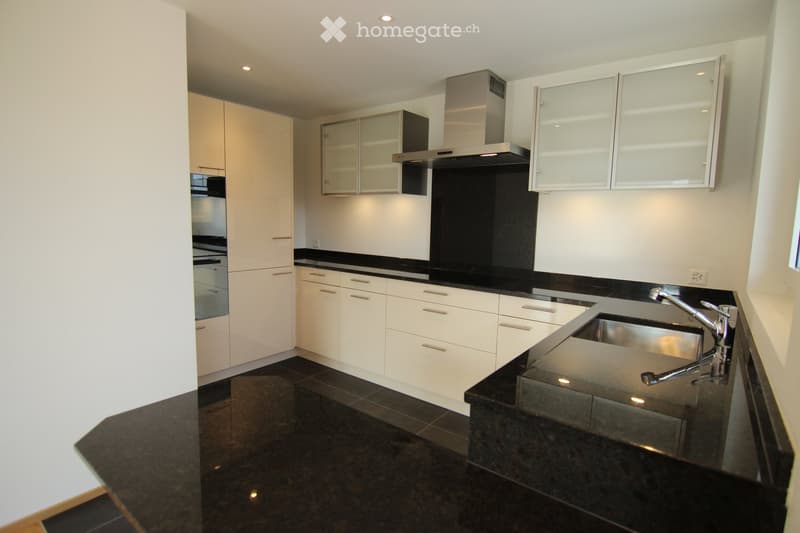 Modern kitchen with white cabinets, black countertops, and stainless steel sink and range hood.