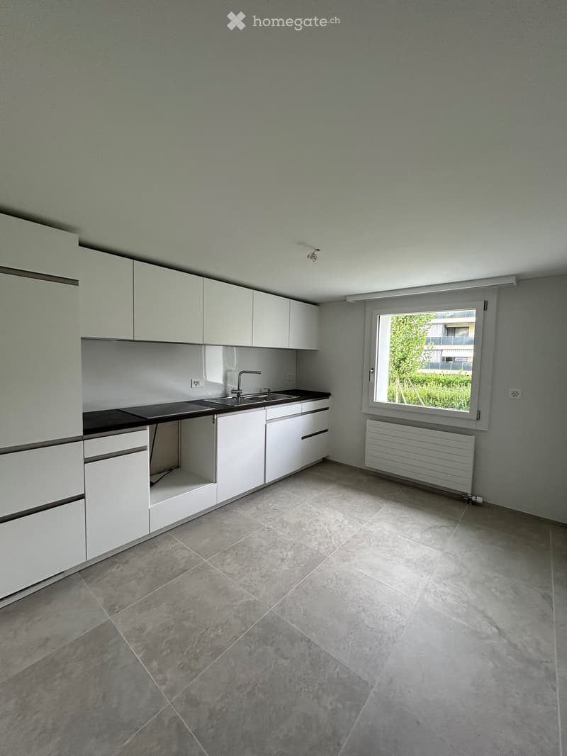 Empty kitchen with white cabinets, a sink, and a window overlooking greenery.
