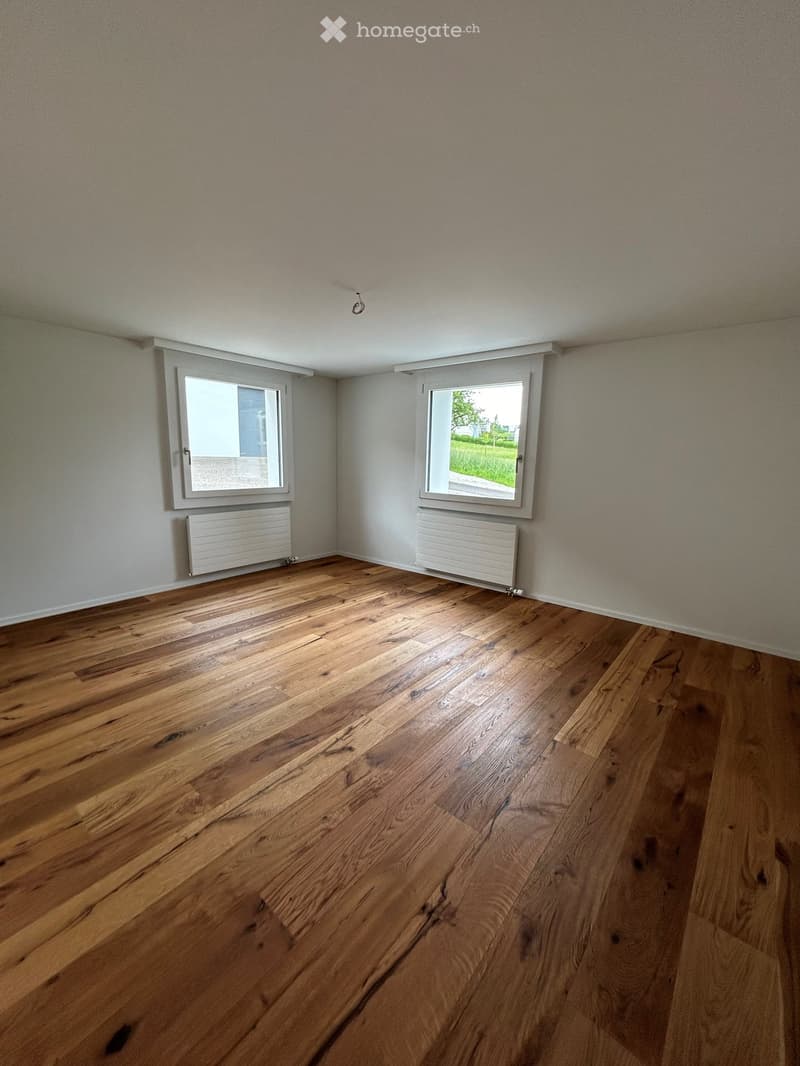 Empty room with wooden flooring, two windows, and radiators on the walls.