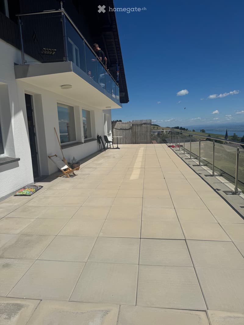 Balcony with tiled floor, glass railing, and outdoor furniture including chairs and a small table.