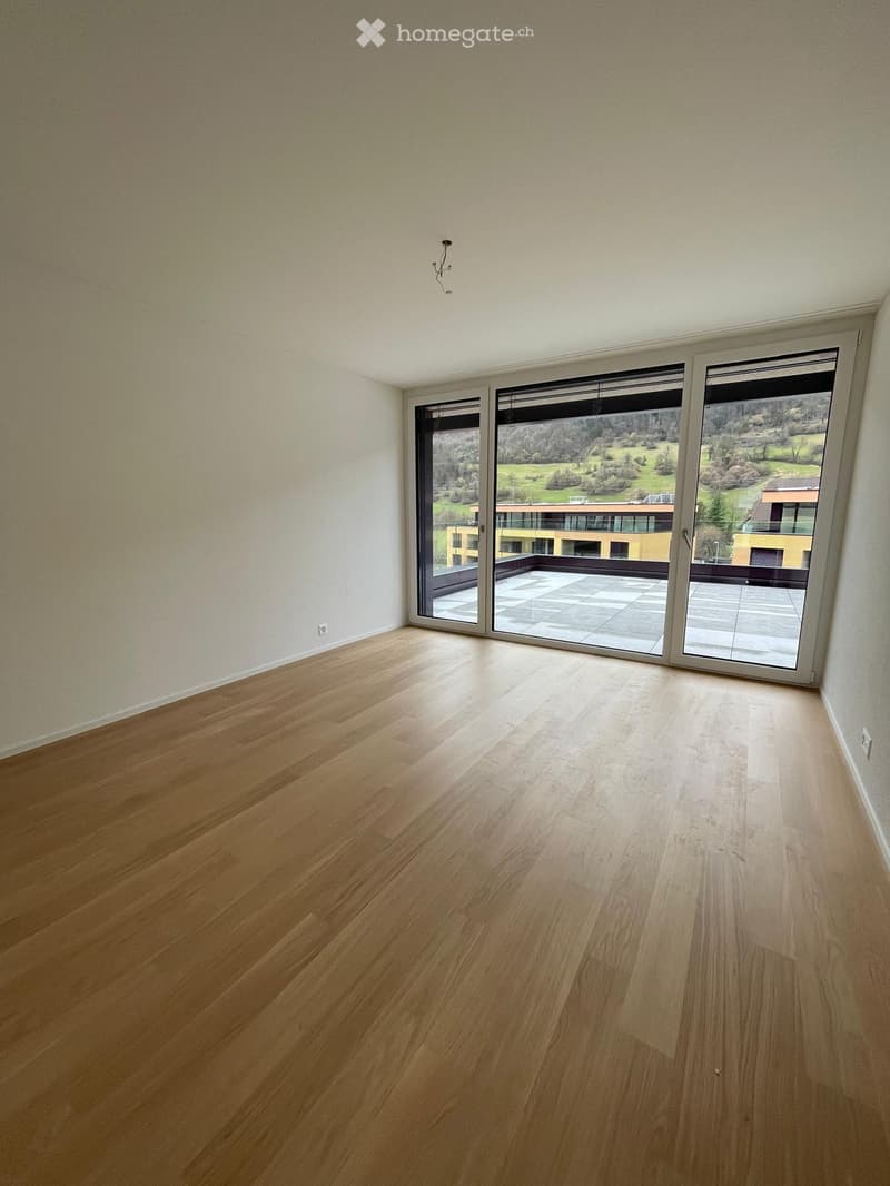 Empty room with wooden flooring, large sliding glass doors leading to a balcony with a scenic view.