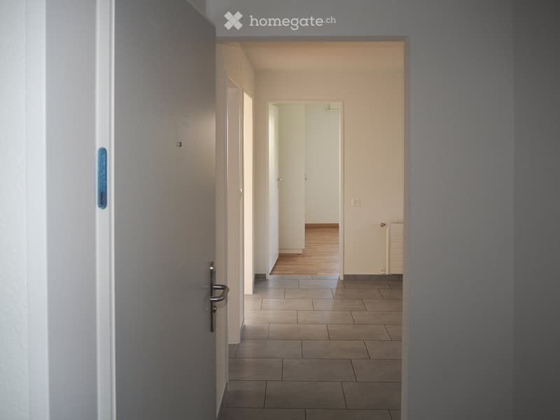 Empty hallway with tiled floor, white walls, and multiple doors leading to other rooms.