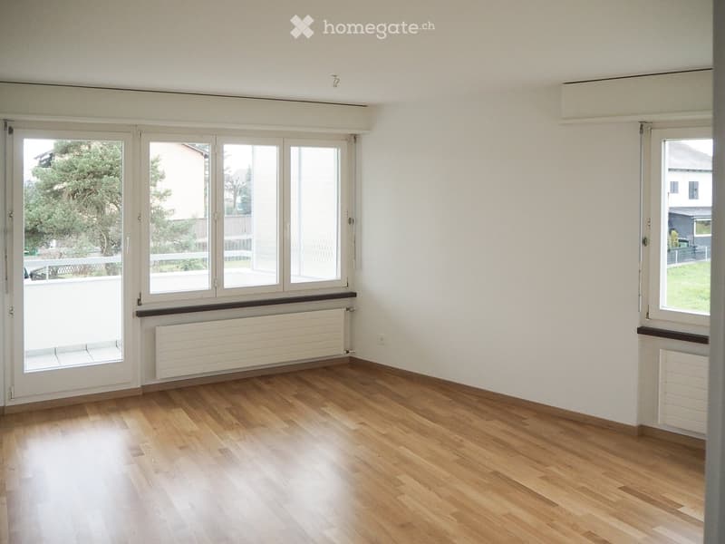 Empty room with wooden flooring, white walls, large windows, and radiators.