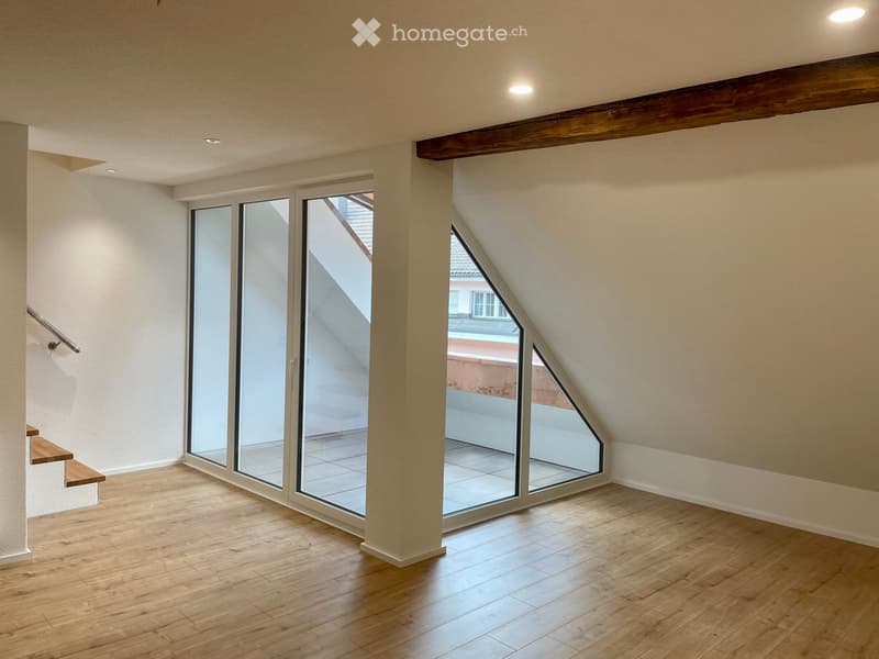 Empty attic room with wooden flooring, large skylight windows, and exposed wooden beams on the ceiling.