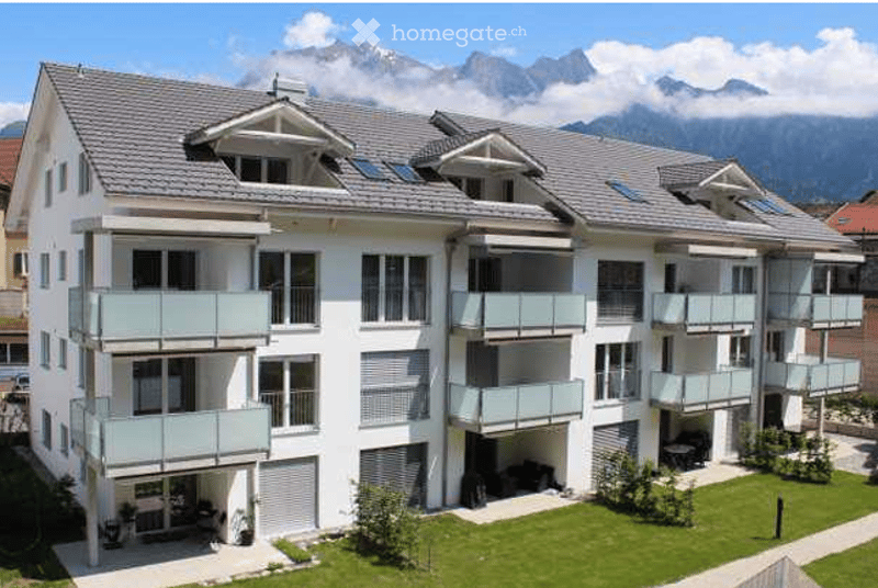 Modern multi-story residential building with multiple balconies and a scenic mountain view in the background.