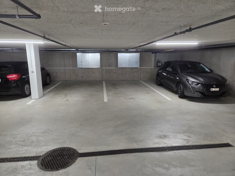 Underground parking area with two parked cars, concrete pillars, and numbered parking spaces.
