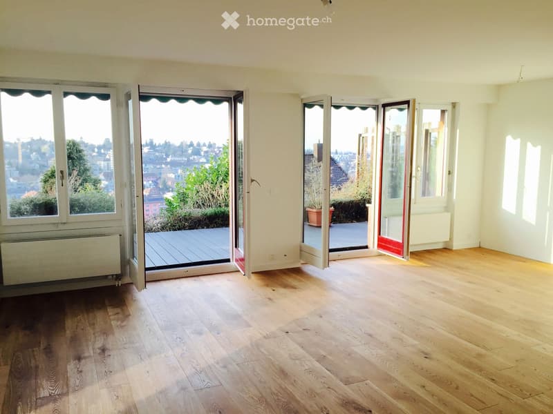 Empty room with wooden flooring, large windows, and sliding glass doors leading to a balcony or terrace area.