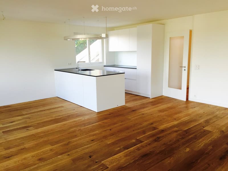 Empty kitchen with white cabinets, a central island, and wooden flooring. No appliances or furniture are present.