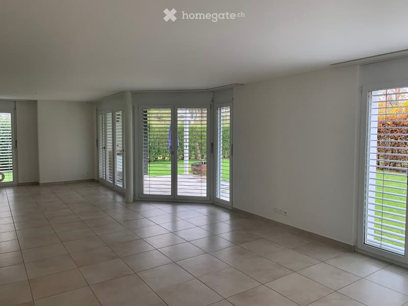 Empty room with tiled floor, white walls, and multiple large sliding glass doors leading to an outdoor area.