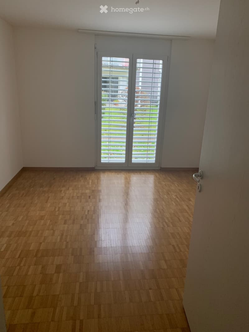 Empty room with wooden flooring, large sliding glass door with blinds, and neutral-colored walls.