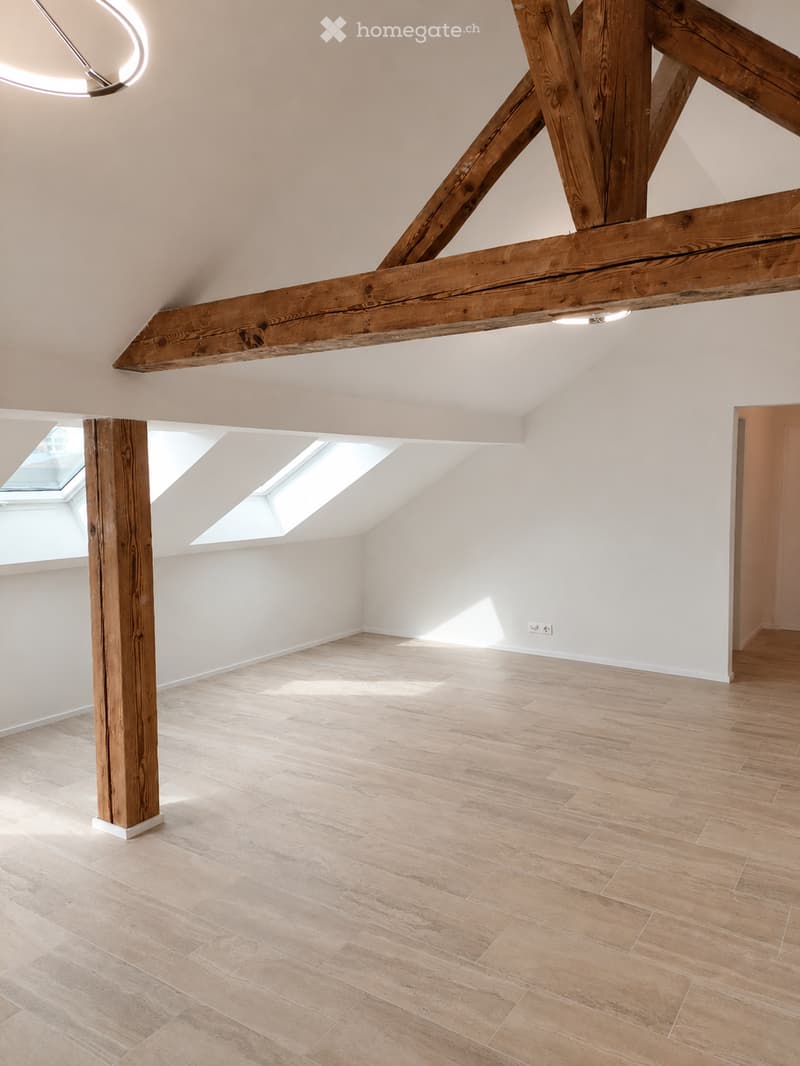Empty attic space with wooden beams, skylights, and light wooden flooring.