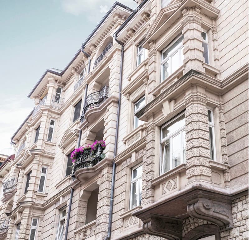 Ornate multi-story building with classical architectural details, large windows, decorative balconies, and a flower planter on one balcony.