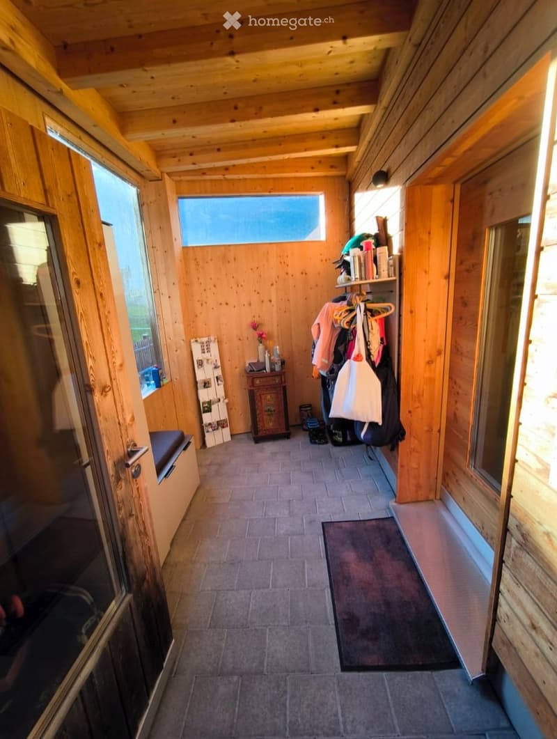 A wooden hallway with a bench, a small cabinet, a shelf with items, and a coat hanger with bags and jackets.