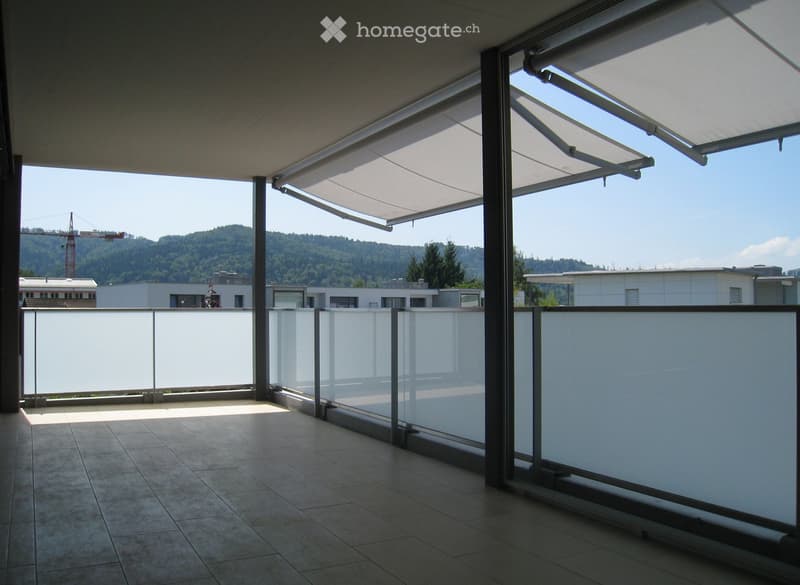 Modern balcony with large retractable awnings, glass railings, and tiled flooring, offering a scenic view of a hilly landscape.