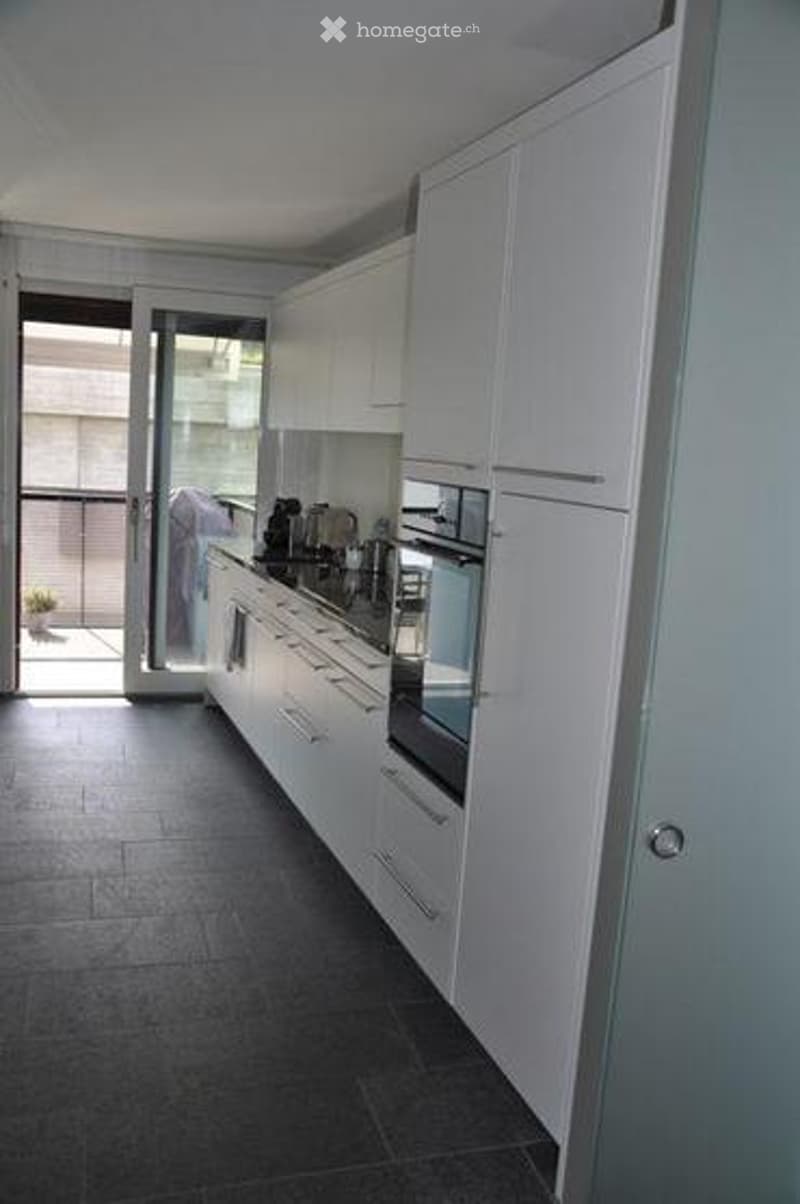 Modern kitchen with white cabinets, stainless steel appliances, and a sliding glass door leading to a balcony.