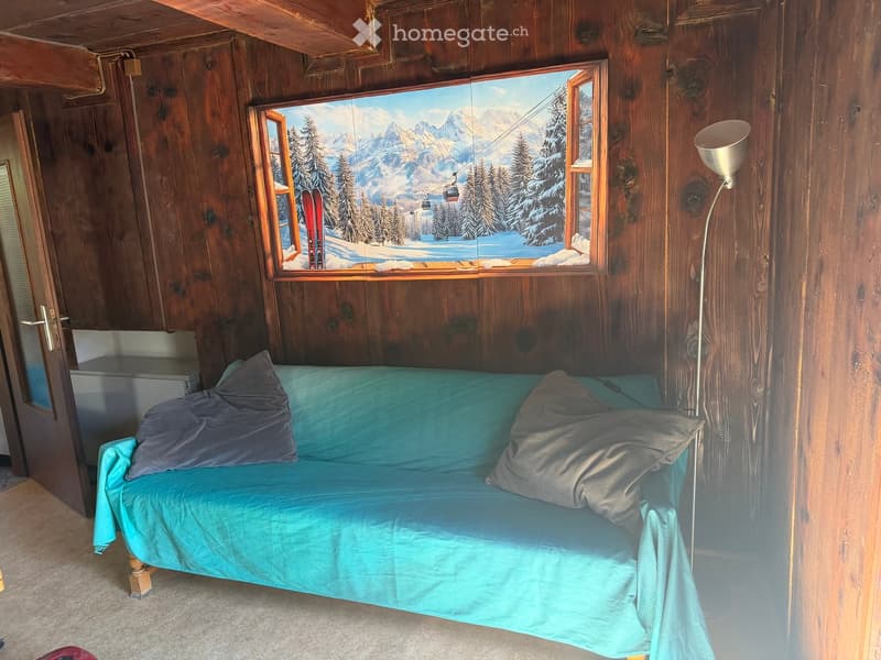 Cozy room with wooden walls, a blue sofa with pillows, a floor lamp, and a large window with a scenic mountain view.