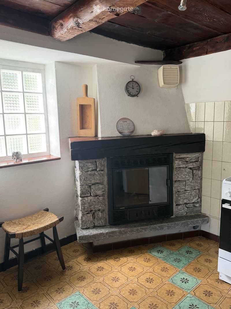Cozy room with exposed wooden beams, stone fireplace, wicker stool, and decorative items on mantel.