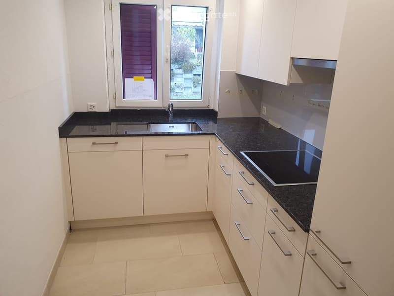 Modern kitchen with white cabinets, black countertops, and stainless steel appliances, including a sink and stove.