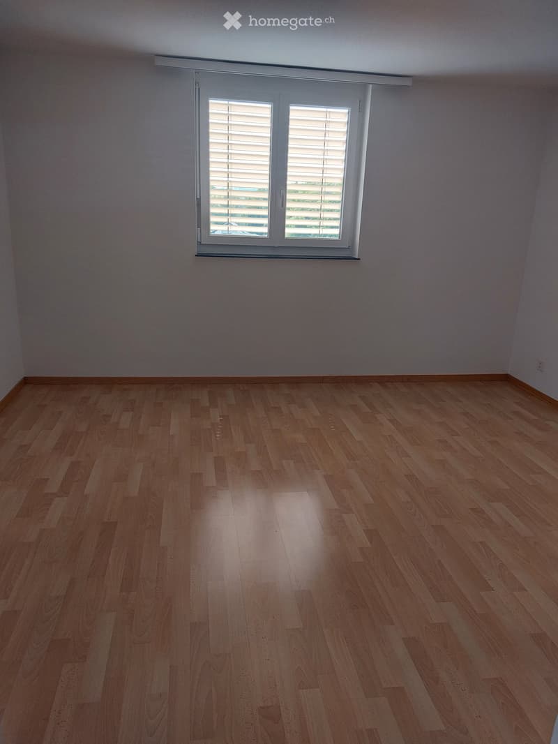 Empty room with wooden flooring and a large window with blinds.