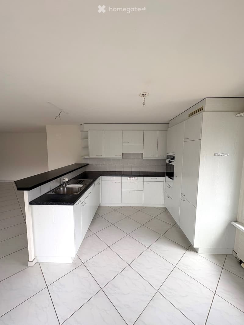 Modern kitchen with white cabinets, black countertops, and a central island. Features a sink, oven, and ample storage space.