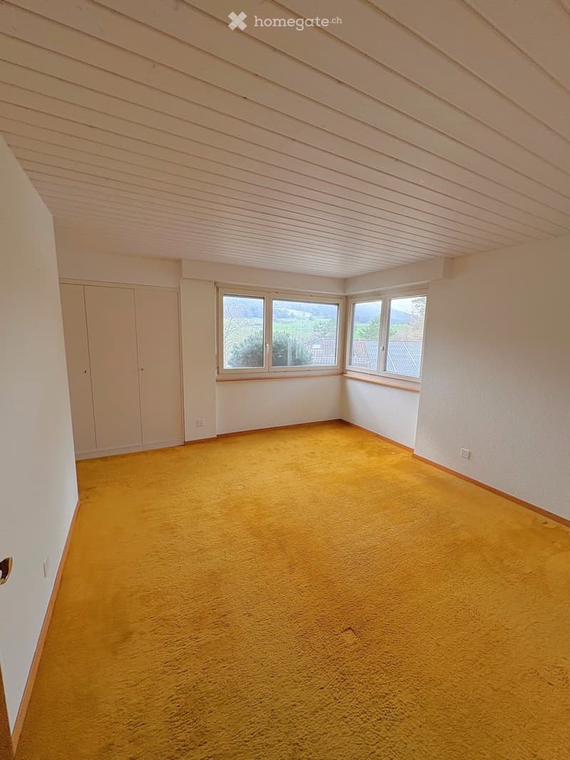 Empty room with yellow carpet, white walls, and large windows offering a view of the landscape.