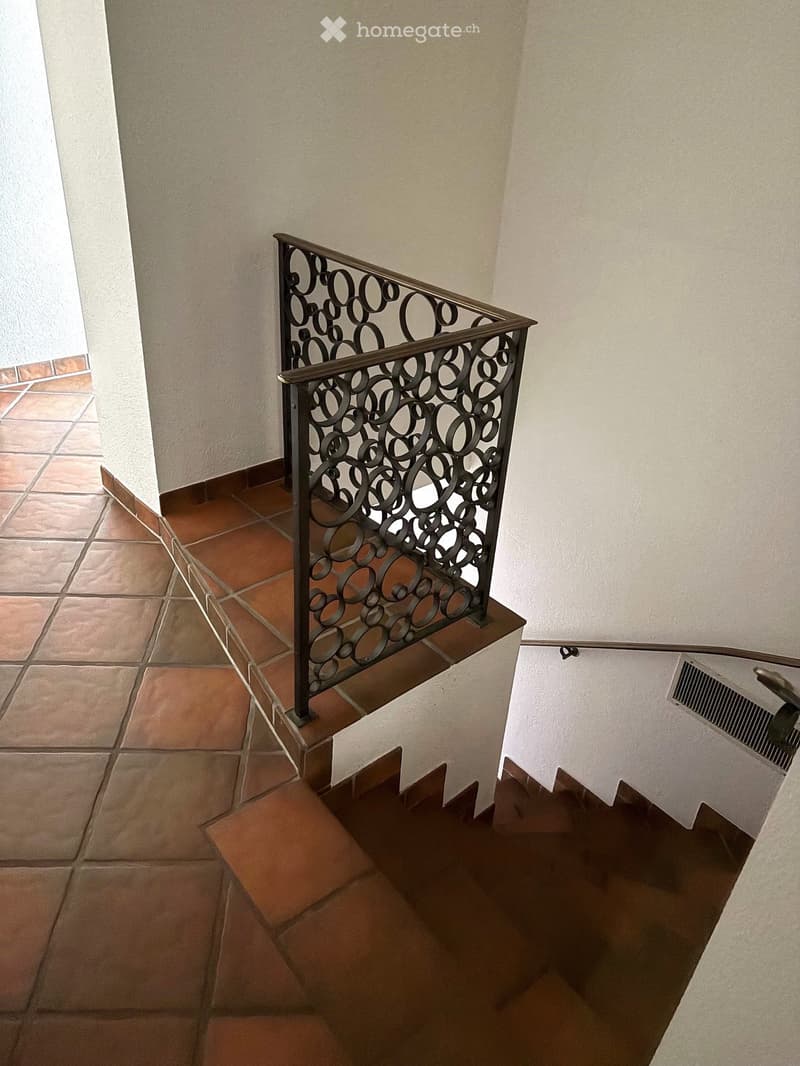 Staircase with a decorative metal railing and tiled steps, leading to an upper level.