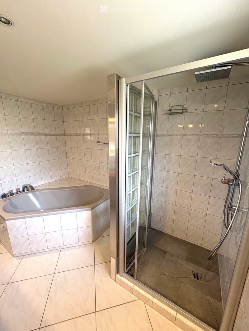 Modern bathroom with a bathtub and a separate shower area, featuring tiled walls and a glass shower enclosure.
