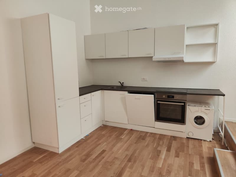 Modern kitchen with white cabinets, black countertops, wooden flooring, and built-in appliances including a sink, oven, dishwasher, and washing machine.