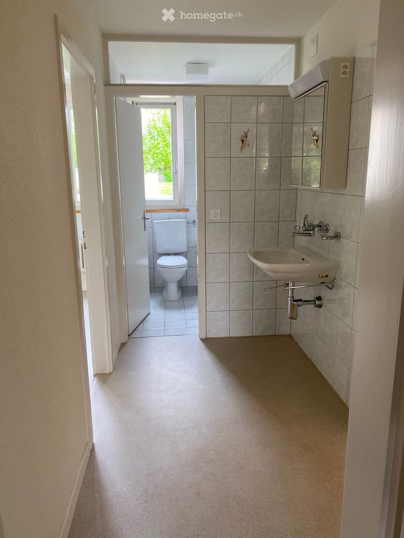 Bathroom with a sink and toilet, tiled walls, and a window providing natural light.