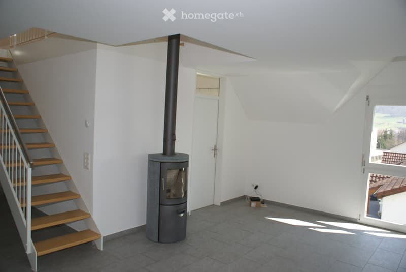 Modern hallway with a staircase leading upwards, a wood-burning stove, and a large window offering a view of the outdoors.