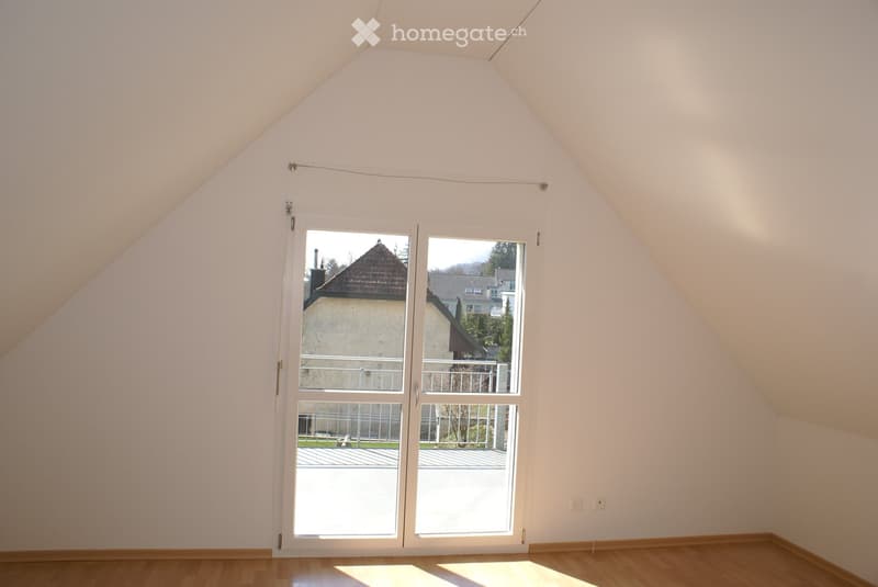 Empty attic room with wooden flooring, white walls, and large sliding glass doors leading to a balcony or outdoor area.