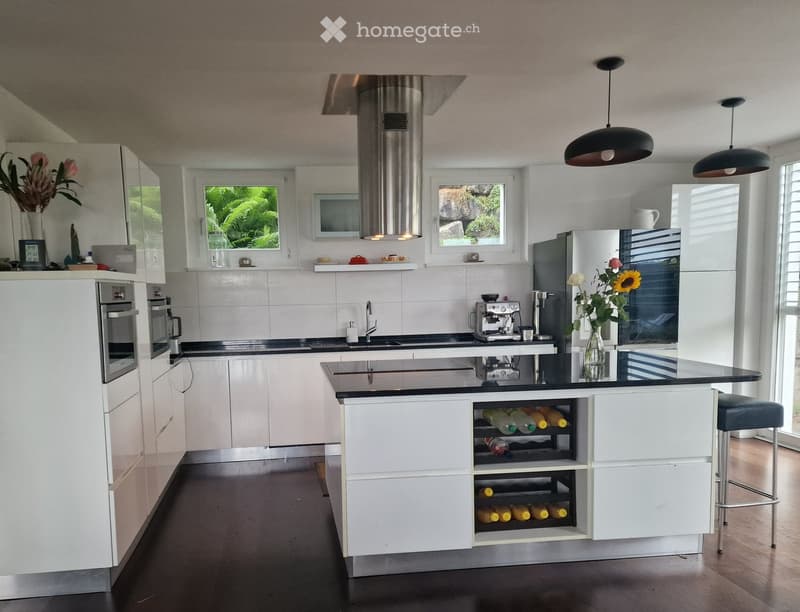 Modern kitchen with white cabinets, black countertops, stainless steel appliances, and a wine rack in the island.