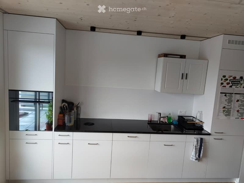 Modern kitchen with white cabinets, black countertop, sink, stove, and various kitchen items including a cutting board, knife, and a towel hanging from a cabinet.