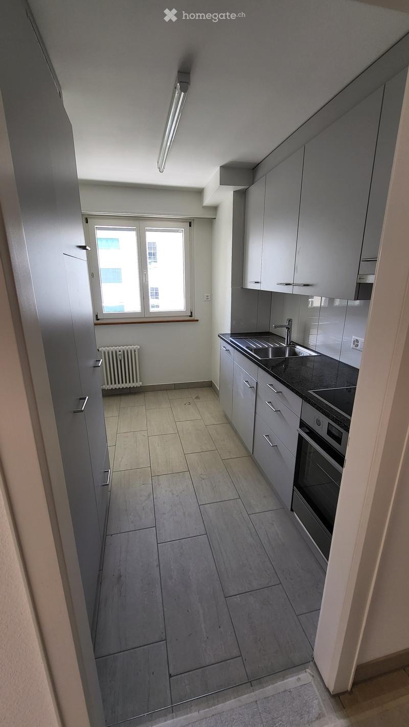 Modern kitchen with grey cabinets, tiled floor, stainless steel sink, and built-in oven. Features a window with a view and a radiator below it.