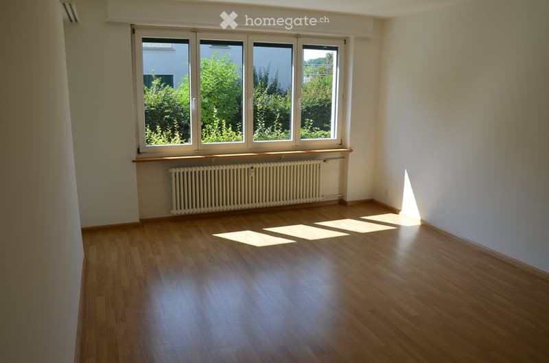 Empty room with wooden flooring, large windows, radiator, and natural light. No furniture or equipment present.