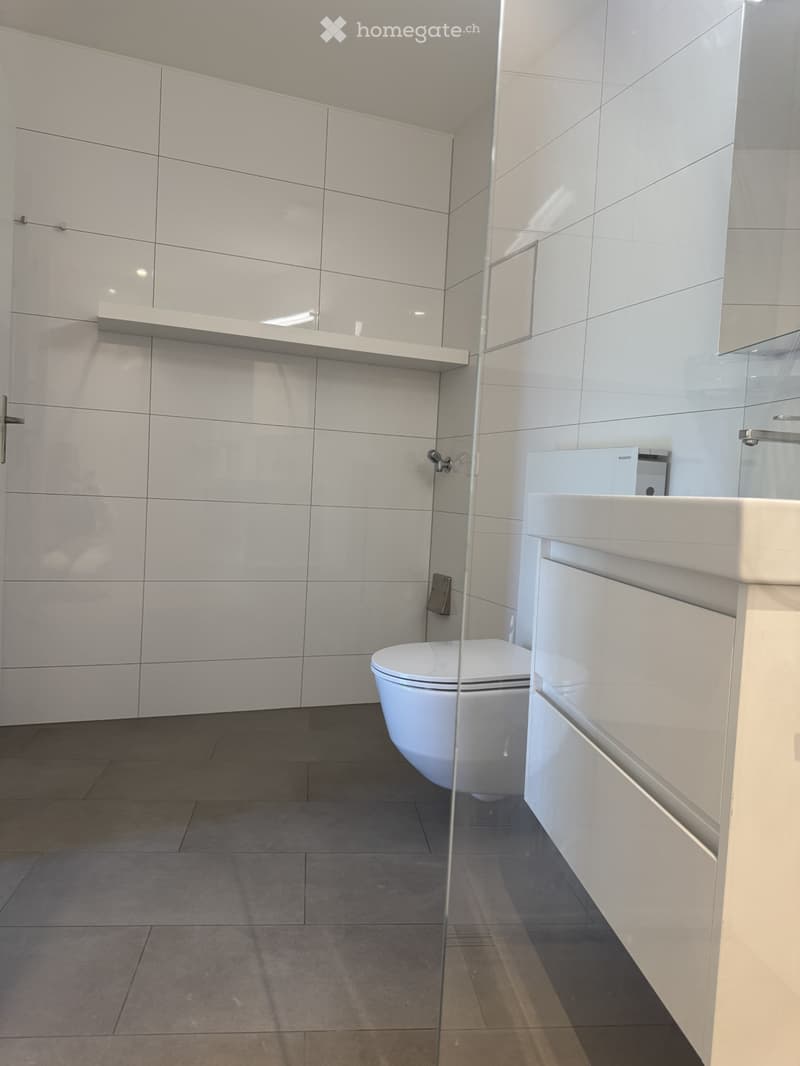 Modern bathroom with white tiles, a toilet, a sink with a cabinet, and a glass shower enclosure.