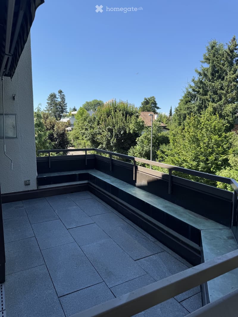 Balcony with tiled floor, metal railing, and steps leading up, overlooking a green, tree-filled area.