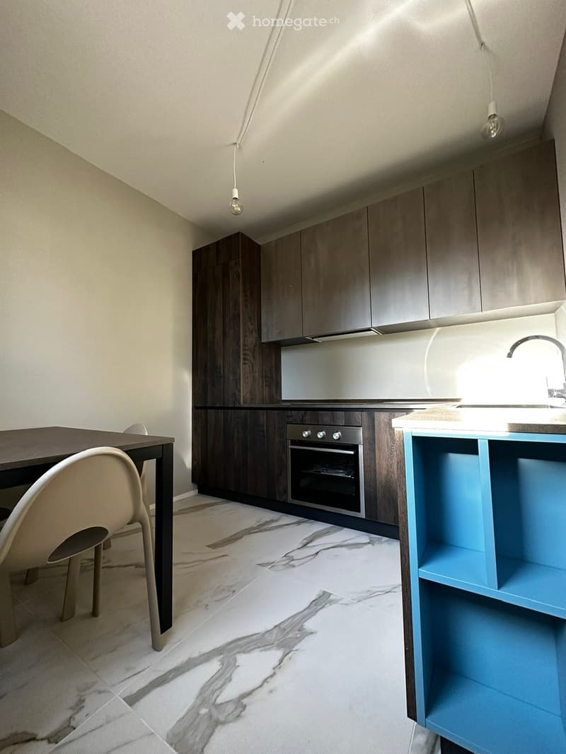 Modern kitchen with dark wood cabinets, marble flooring, a sink, an oven, and a dining area with a table and chairs.