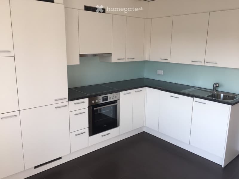 Modern kitchen with white cabinets, black countertops, and stainless steel appliances including an oven and sink.