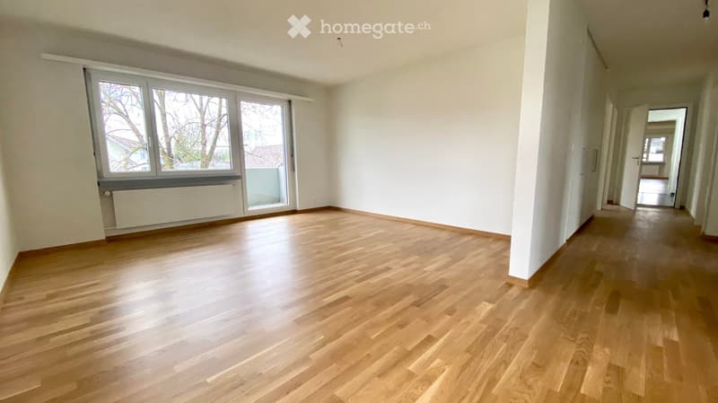Empty room with wooden flooring, white walls, large windows, and a radiator. No furniture or equipment present.