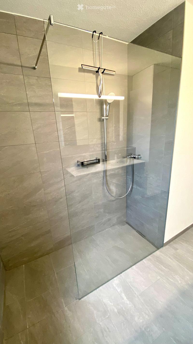 a glass enclosure, large white tiles, metal shower fixture