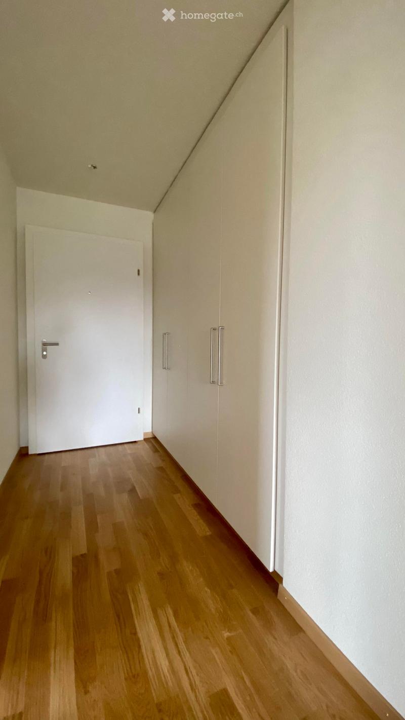Empty hallway with wooden flooring, white walls, and a closed door at the end.